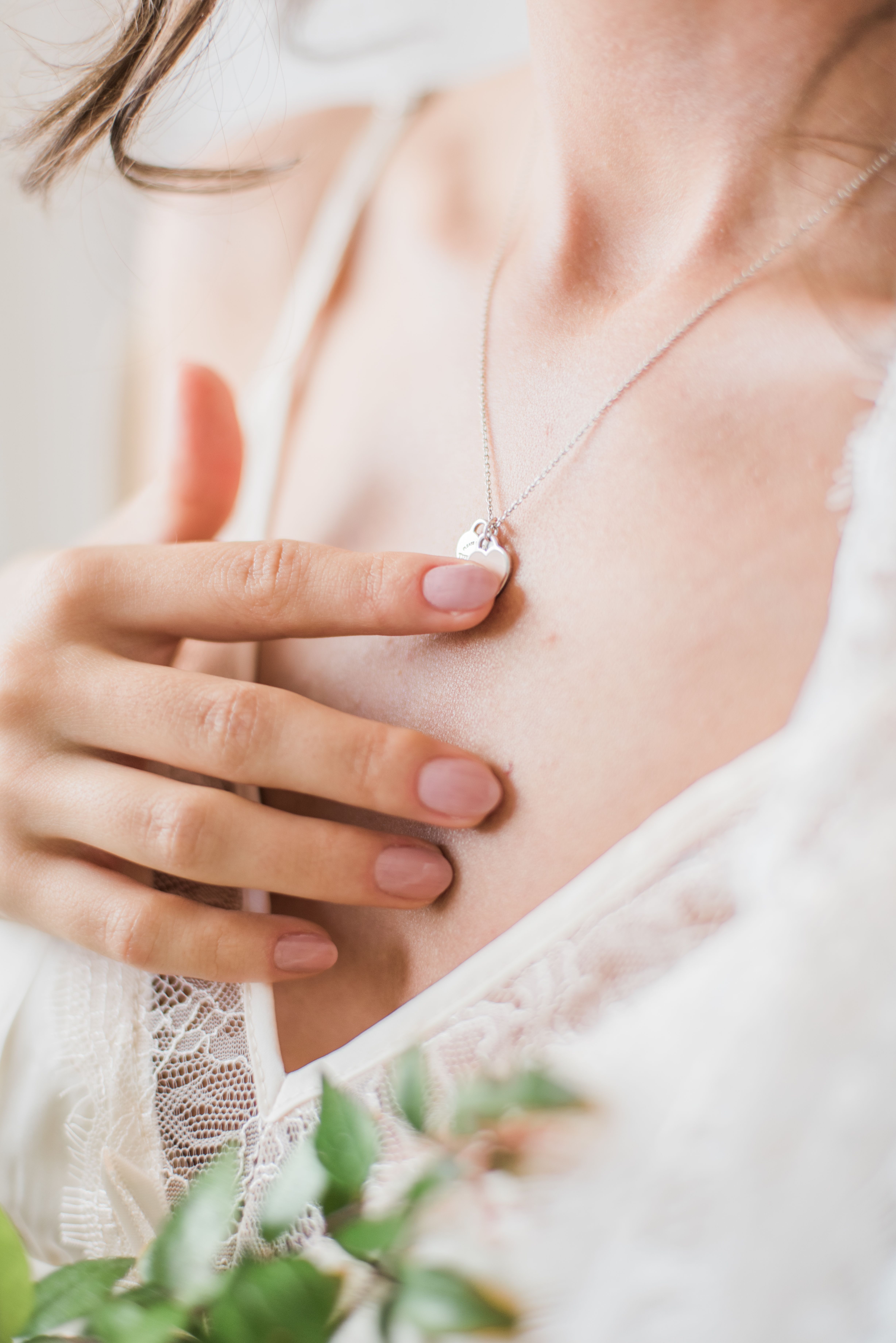 Braut mit zarter Herzkette an der Hand vor Spitzenkleid