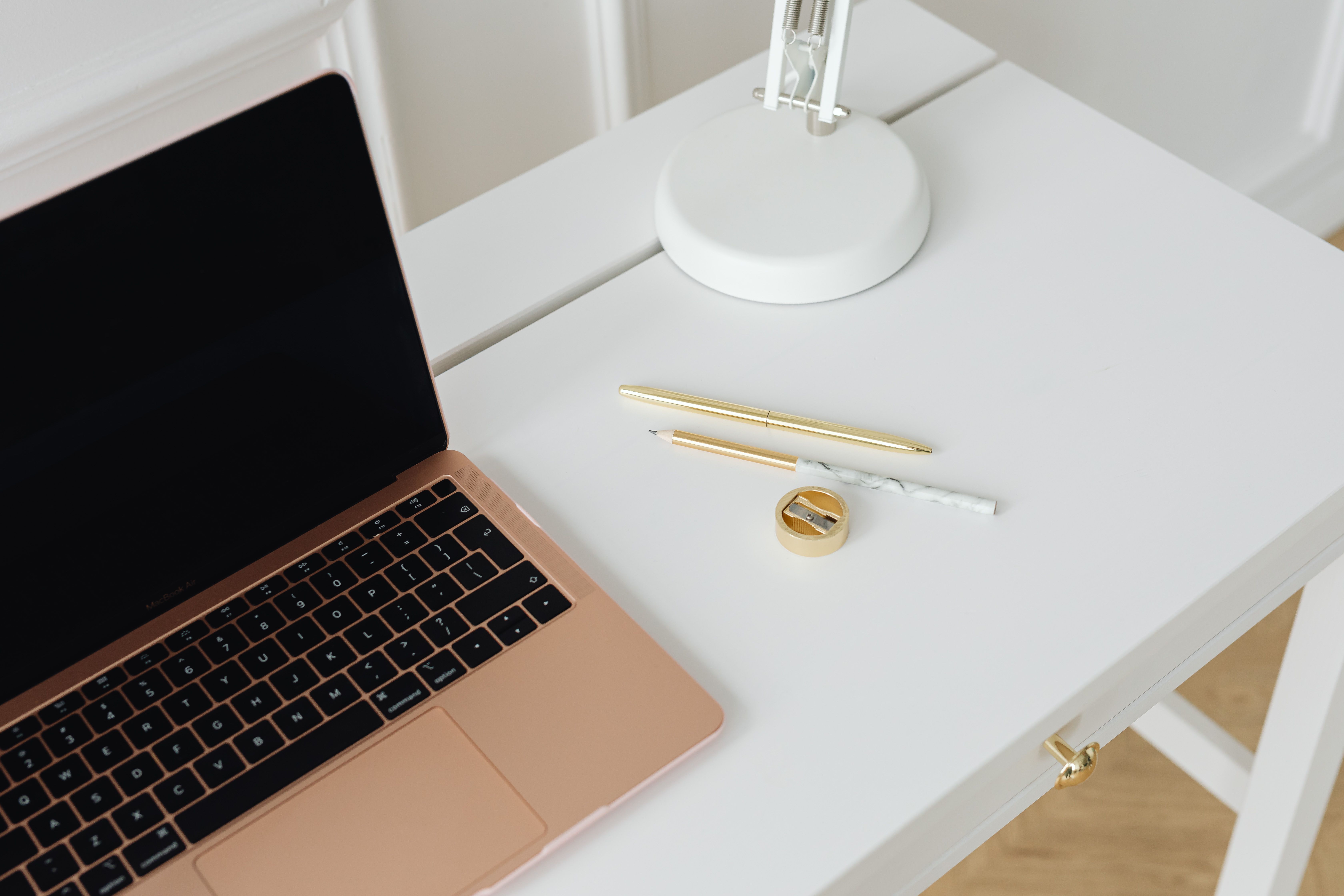 Heller Schreibtisch mit Laptop, goldenem Stift und Notizutensilien